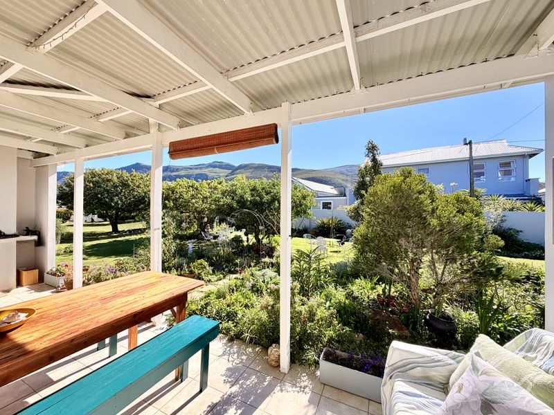 A covered outdoor patio featuring a corrugated roof and tiled flooring, overlooking a lush garden with mountain views.