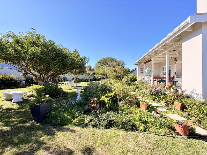 A well-maintained rear garden featuring a lush lawn, established trees, and a covered patio area attached to the main house structure.
