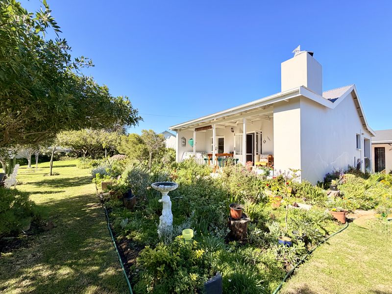A well-maintained rear exterior view of the house featuring a covered patio, a prominent chimney, and a lush, established garden with lawn.