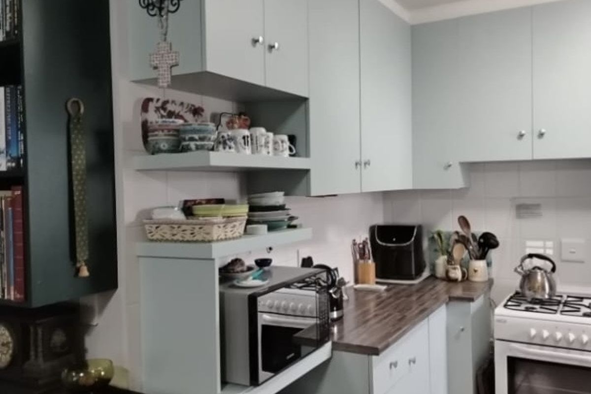 A functional kitchen featuring light blue cabinetry, dark laminate countertops, a tiled backsplash, and a freestanding stove with tiled flooring.