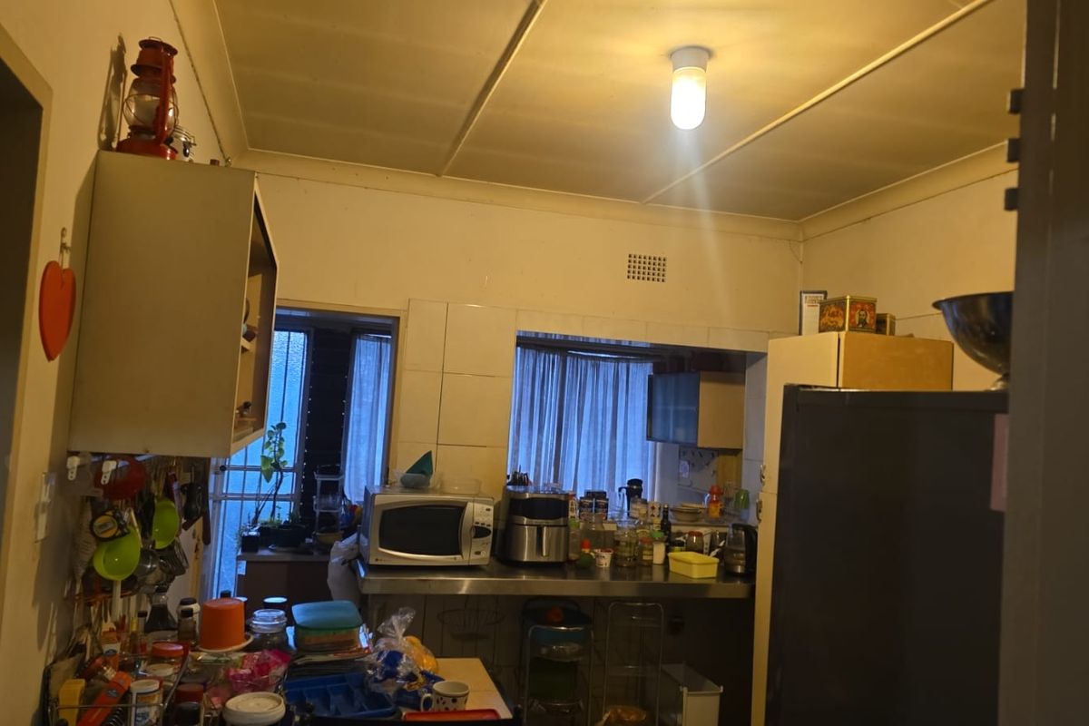 A functional kitchen space featuring built-in cabinetry, a stainless steel countertop, and tiled splashback, currently showing signs of age and wear.