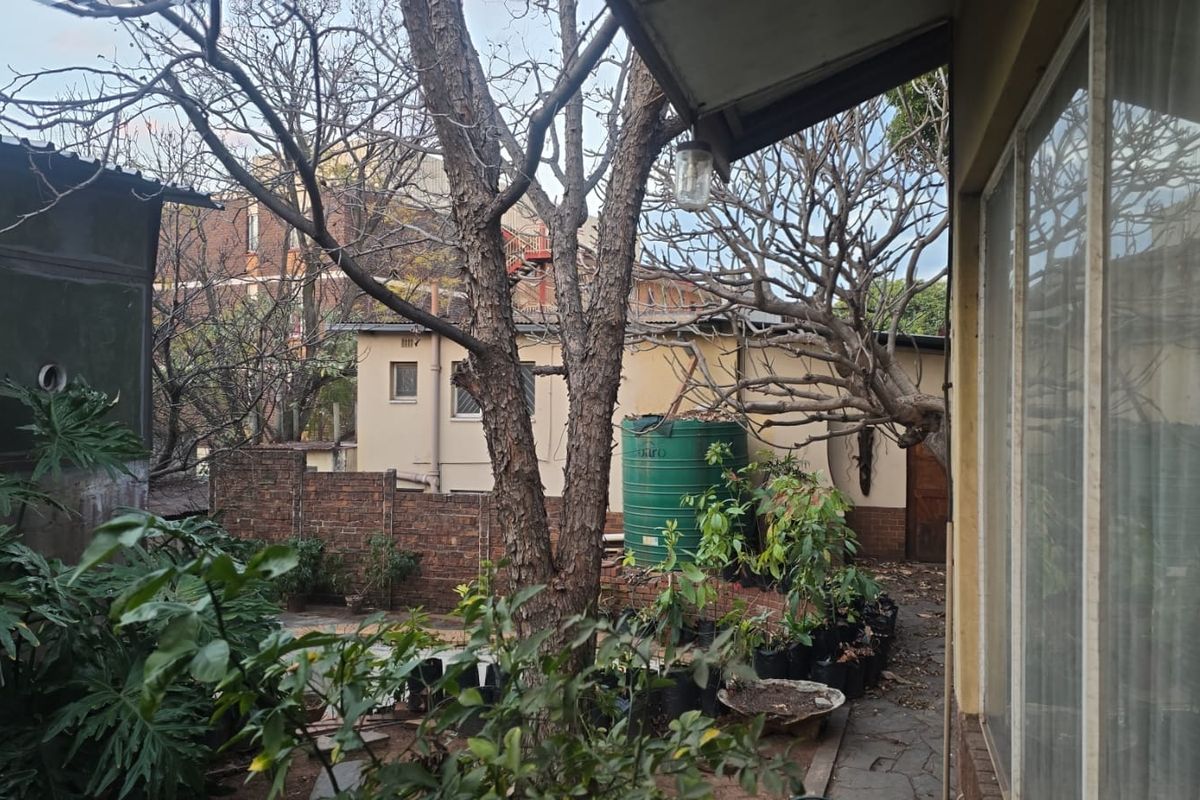 A view of the rear garden area featuring a paved patio, brick boundary wall, and a water storage tank.