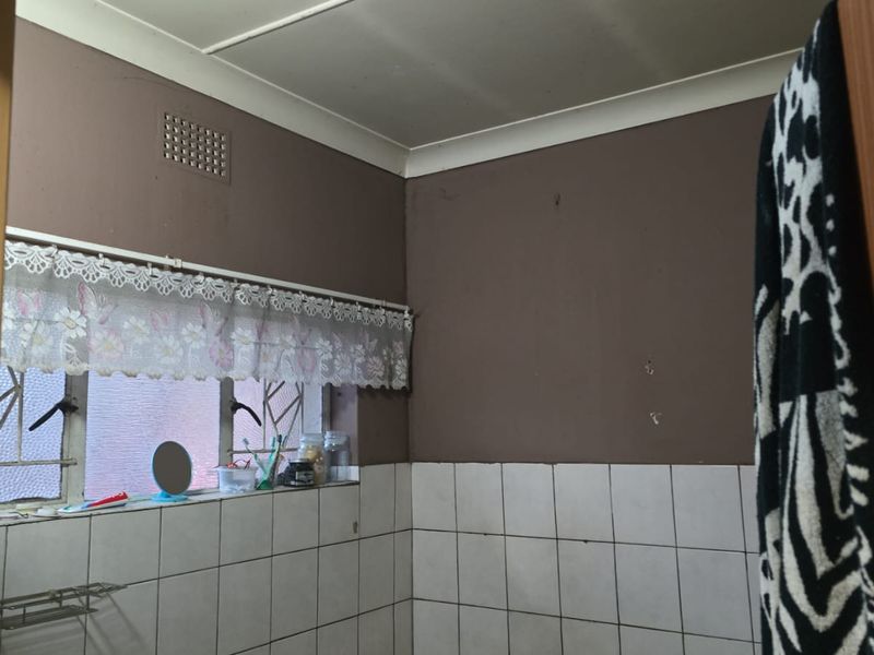 A bathroom featuring partially tiled walls and a ventilation grille, currently requiring cosmetic updates and maintenance to improve its overall condition.