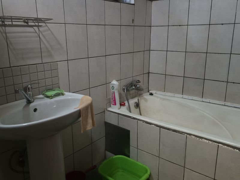 A functional bathroom featuring a pedestal basin and a built-in bathtub with full-height wall tiling.