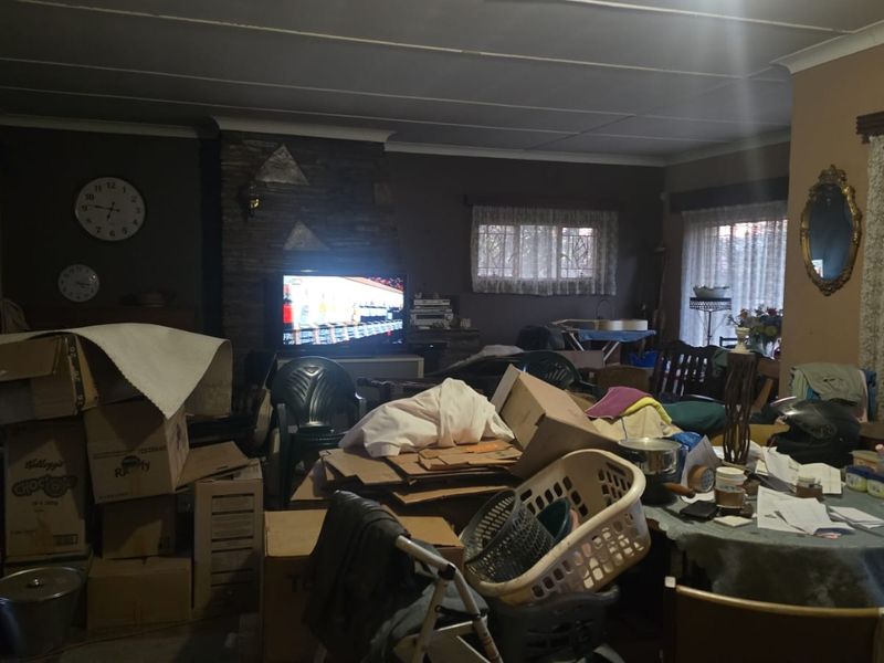 A living room featuring a stone-clad fireplace and coved ceiling, currently cluttered with personal belongings and moving boxes.