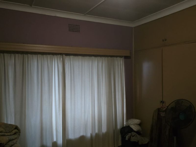A bedroom featuring built-in cupboards and a window with curtains. The room requires updated finishes and improved lighting to enhance its appeal.