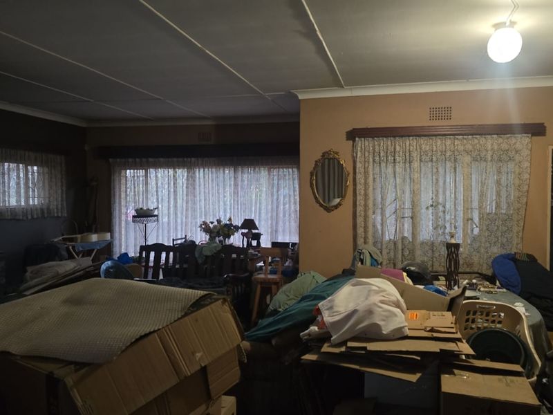 A spacious living area featuring large windows with security bars and traditional ceiling panels, offering potential for a modern renovation.