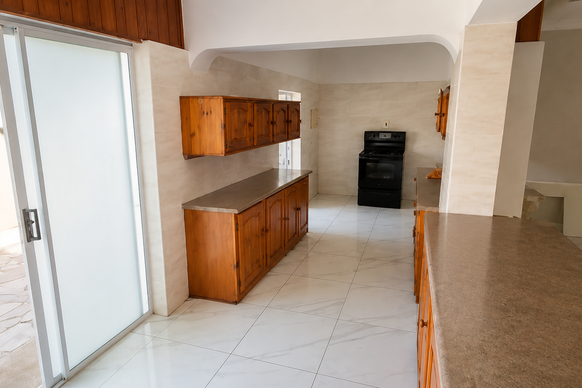 A spacious, empty kitchen featuring wooden cabinetry, stone-look countertops, a freestanding stove, and direct access to an outdoor patio area through sliding glass doors.