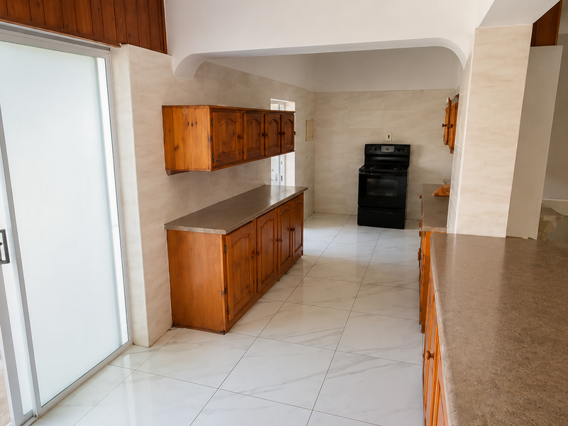 A spacious, empty kitchen featuring wooden cabinetry, stone-look countertops, a freestanding stove, and direct access to an outdoor patio area through sliding glass doors.