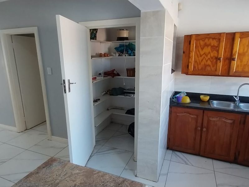 Kitchen area featuring wooden cabinetry, granite countertops, a double bowl sink, and an adjacent walk-in pantry with tiled flooring throughout.