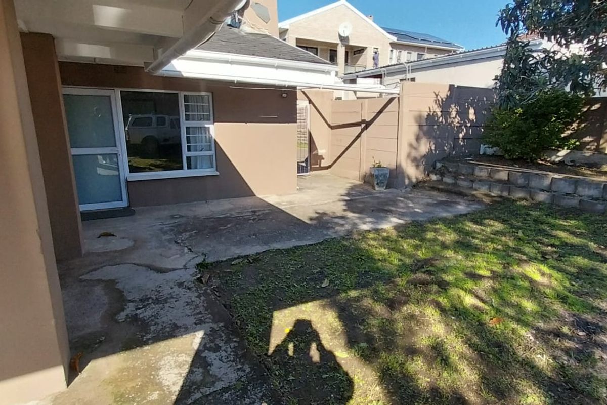 Rear exterior view featuring a concrete patio area, boundary wall, and small garden space with potential for landscaping improvements.