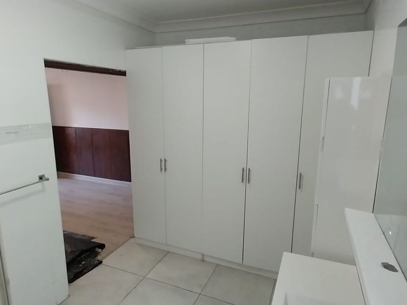 A clean, modern bathroom featuring a glass shower enclosure, ample built-in storage cupboards, and a vanity mirror with tiled finishes throughout.