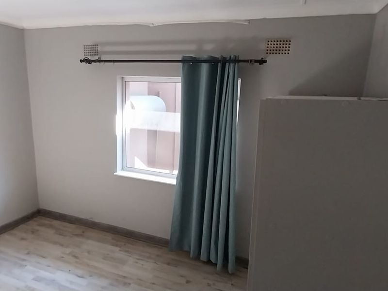 A simple, neutral-toned bedroom featuring laminate flooring and a window with a curtain rod, offering a clean and blank canvas for personalization.