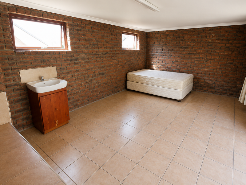 Spacious bedroom featuring exposed brick walls, tiled flooring, a built-in vanity basin, and direct access to the outdoors via french doors.