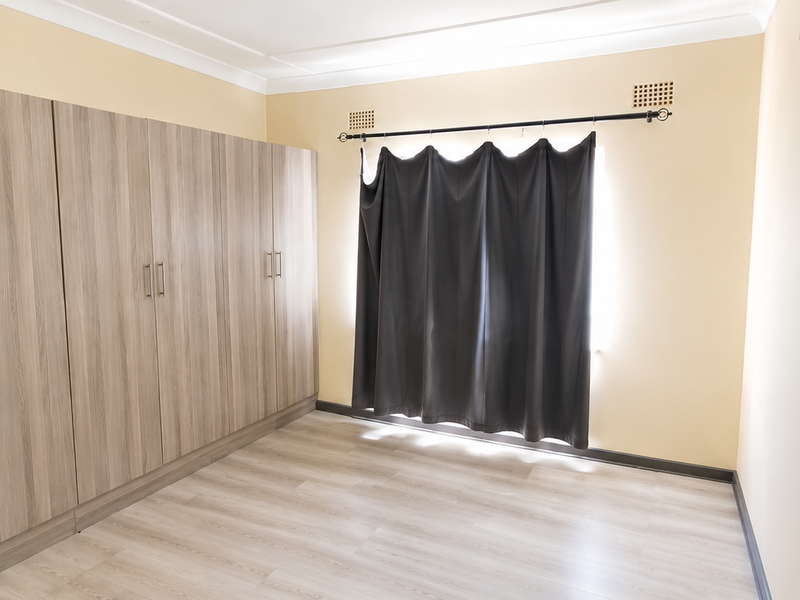 A clean, empty bedroom featuring light-toned laminate flooring and extensive built-in wooden cupboards, providing ample storage space.