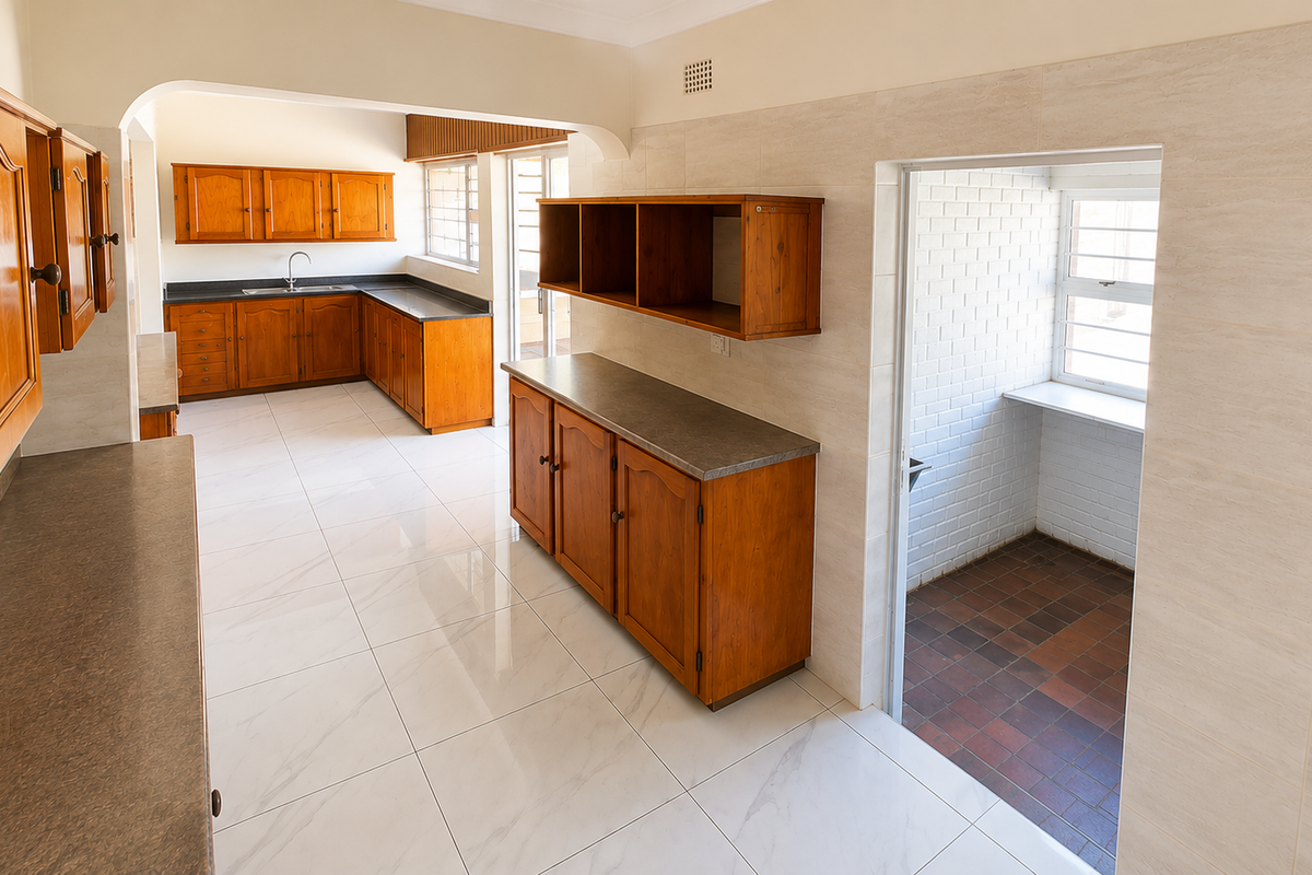 A spacious, empty kitchen featuring wooden cabinetry, laminate countertops, and light-colored floor tiles, with an adjacent utility area and arched transition.