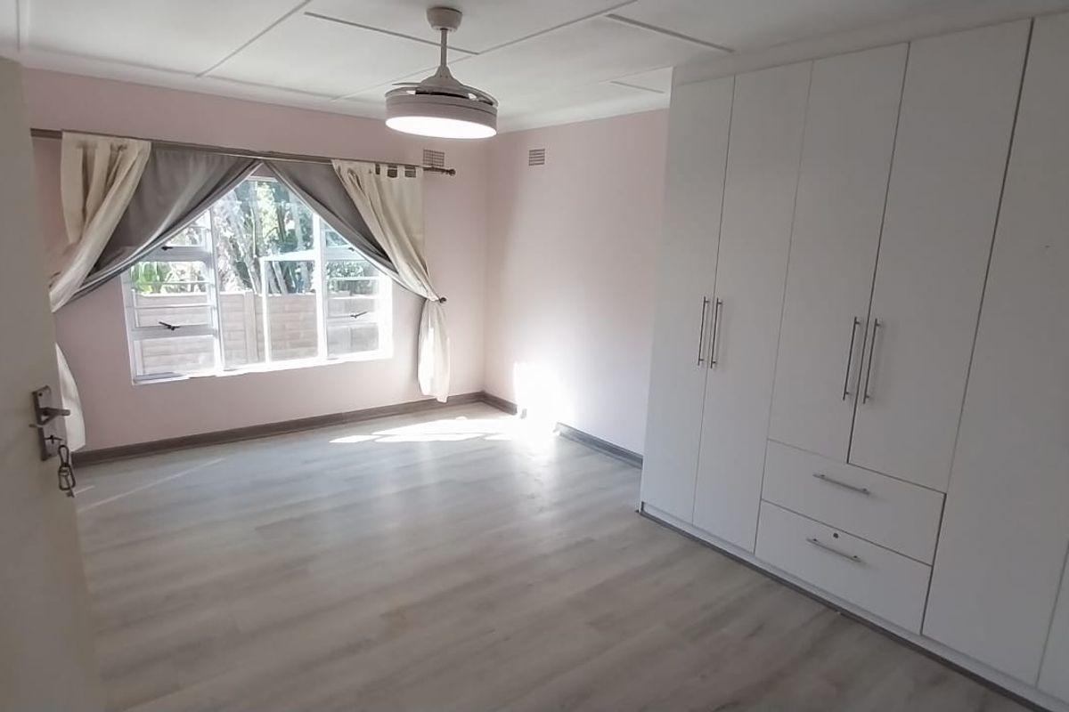 A bright, empty bedroom featuring modern laminate flooring, built-in white cupboards, and a ceiling fan, offering a clean and neutral space.