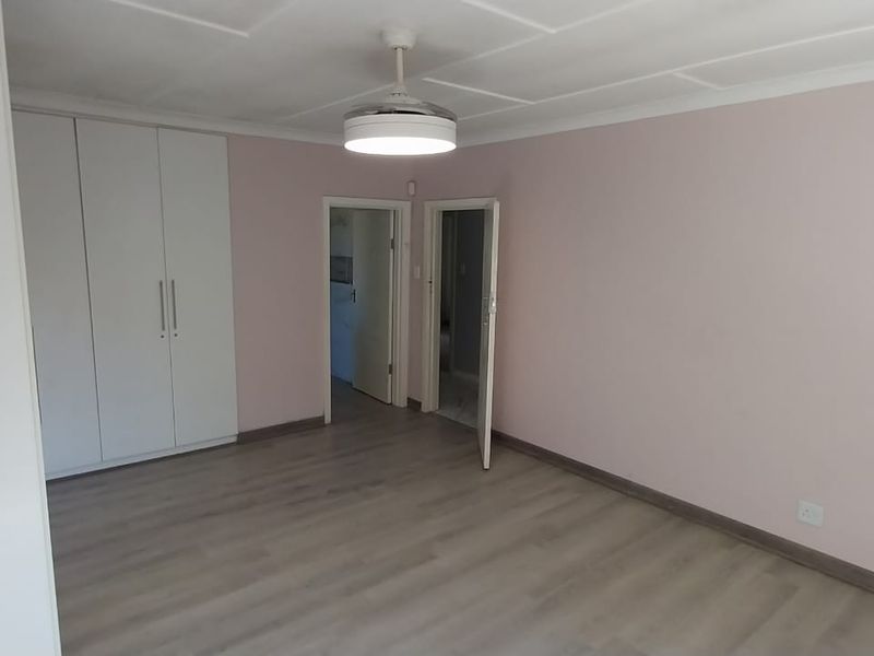 A clean, empty bedroom featuring light laminate flooring, built-in cupboards, and a central ceiling fan light fixture.