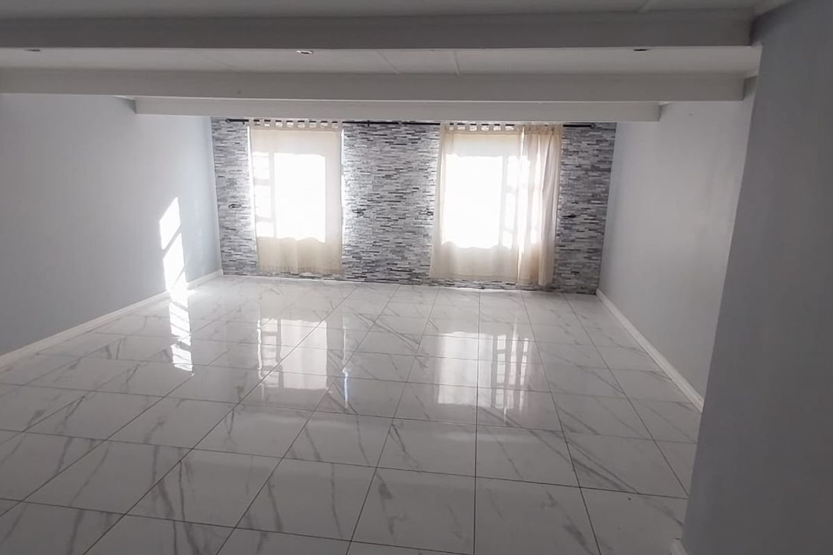 A spacious, empty living area featuring polished marble-look floor tiles, a textured stone-cladding feature wall, and exposed ceiling beams.