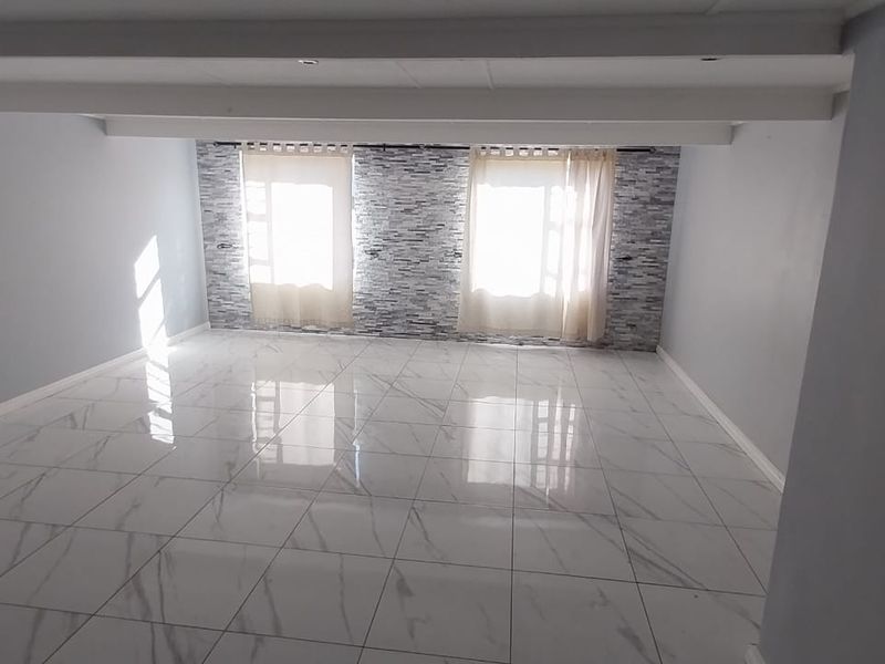 A spacious, empty living area featuring polished marble-look floor tiles, a textured stone-cladding feature wall, and exposed ceiling beams.