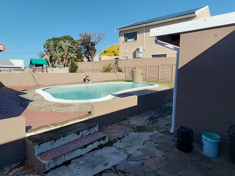 Outdoor pool area featuring a swimming pool, paved surround, and boundary wall, requiring some maintenance to the paving and steps.