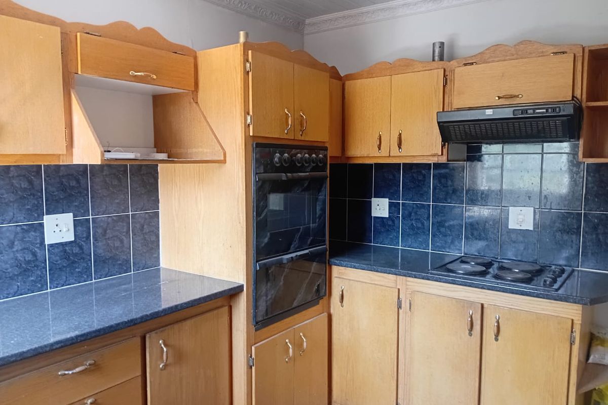 A functional kitchen featuring traditional wooden cabinetry, dark tiled backsplash, built-in eye-level oven, and electric hob with an integrated extractor fan.