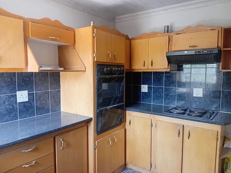 A functional kitchen featuring traditional wooden cabinetry, dark tiled backsplash, built-in eye-level oven, and electric hob with an integrated extractor fan.