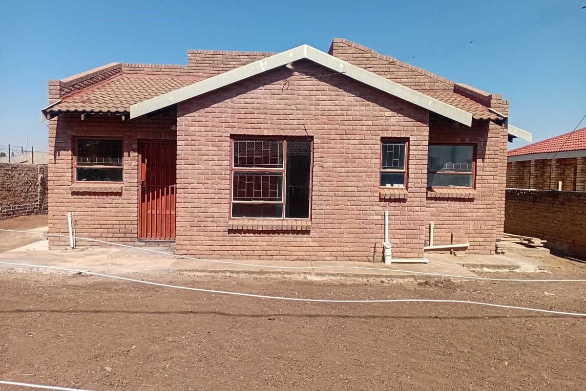 A rear view of a face brick house featuring a tiled roof, security bars on windows, and an unfinished garden area.