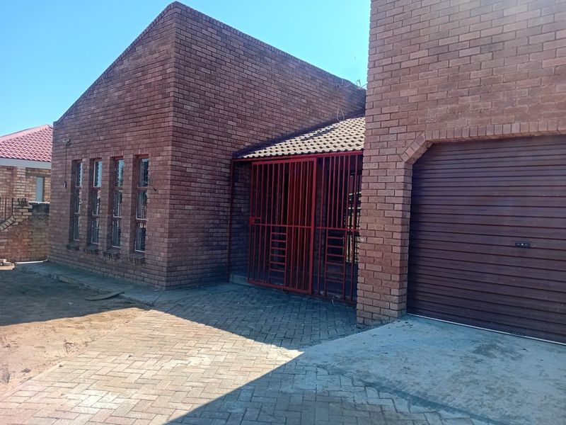 Front exterior view of a face brick house featuring a paved driveway, garage, and secure entrance gate.