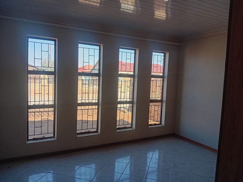 An empty living room featuring tiled flooring, a tongue and groove ceiling, and four large windows fitted with security bars.
