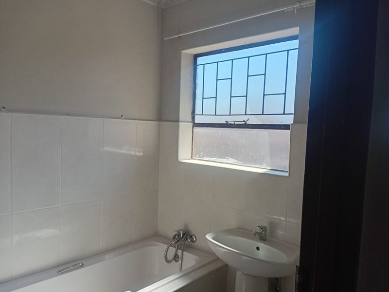 A functional bathroom featuring a standard bathtub, pedestal basin, and tiled walls, currently vacant and ready for updates.