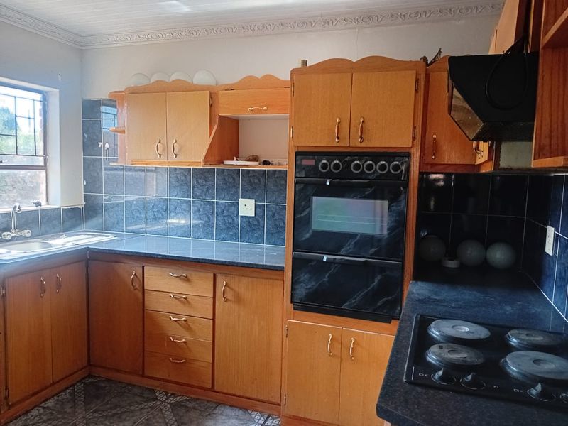 A functional kitchen featuring built-in wooden cabinetry, a double wall oven, electric hob, and tiled finishes, offering a classic layout ready for modernization.