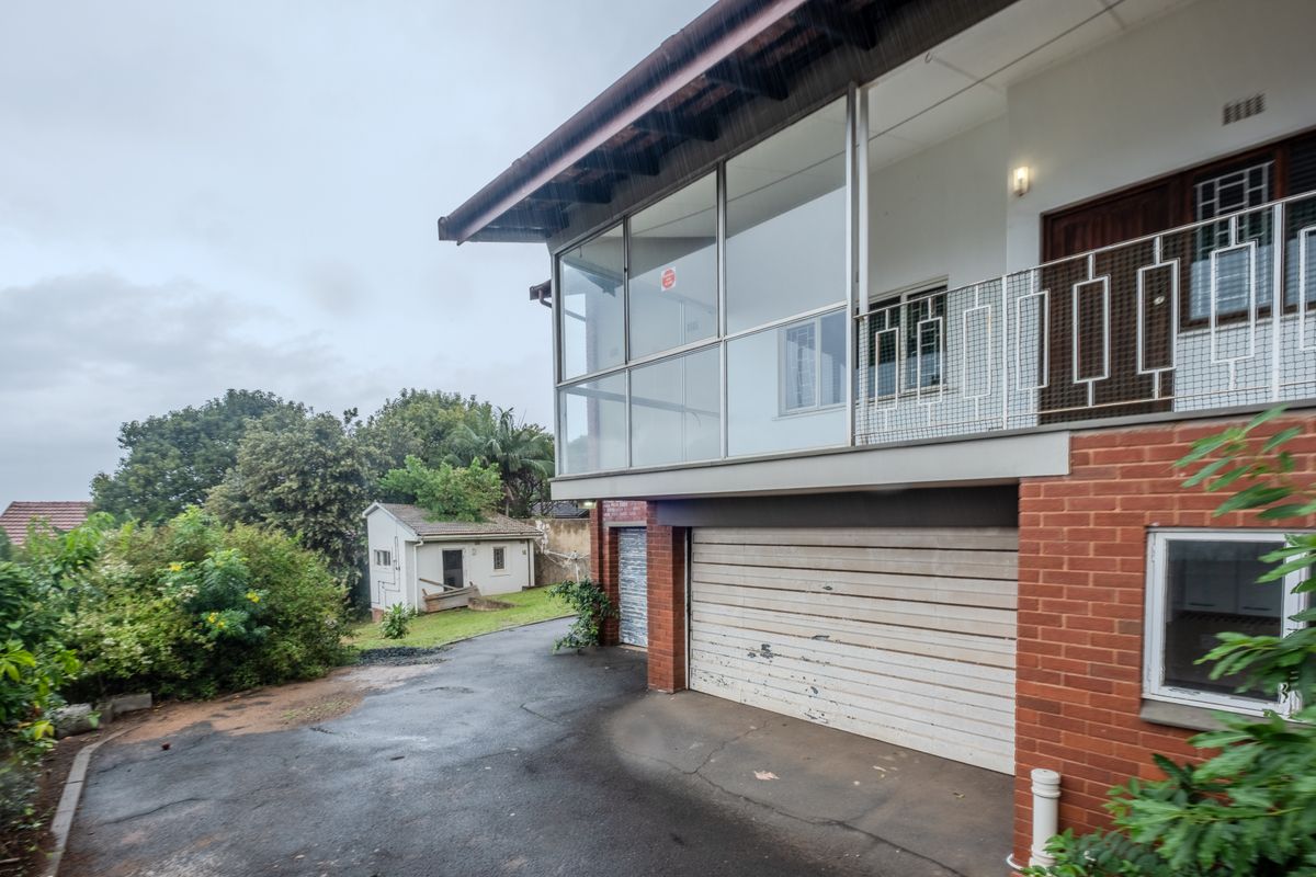 Rear view of the property featuring an enclosed balcony, brick facade, metal garage door, and a paved driveway leading to a separate outbuilding.
