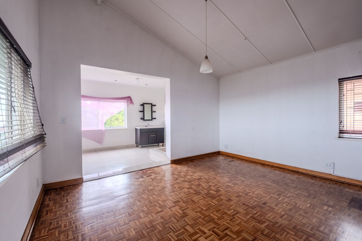 An empty bedroom featuring parquet flooring and an adjoining en-suite area with a vanity unit, offering a blank canvas for renovation.