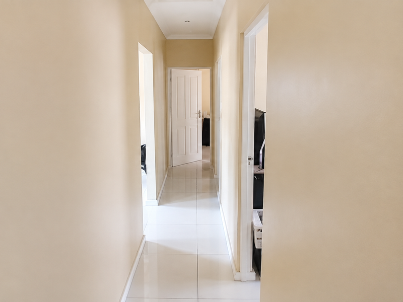 A bright, neutral-toned hallway featuring clean tiled flooring and multiple internal door access points, providing a clear transition between living spaces.