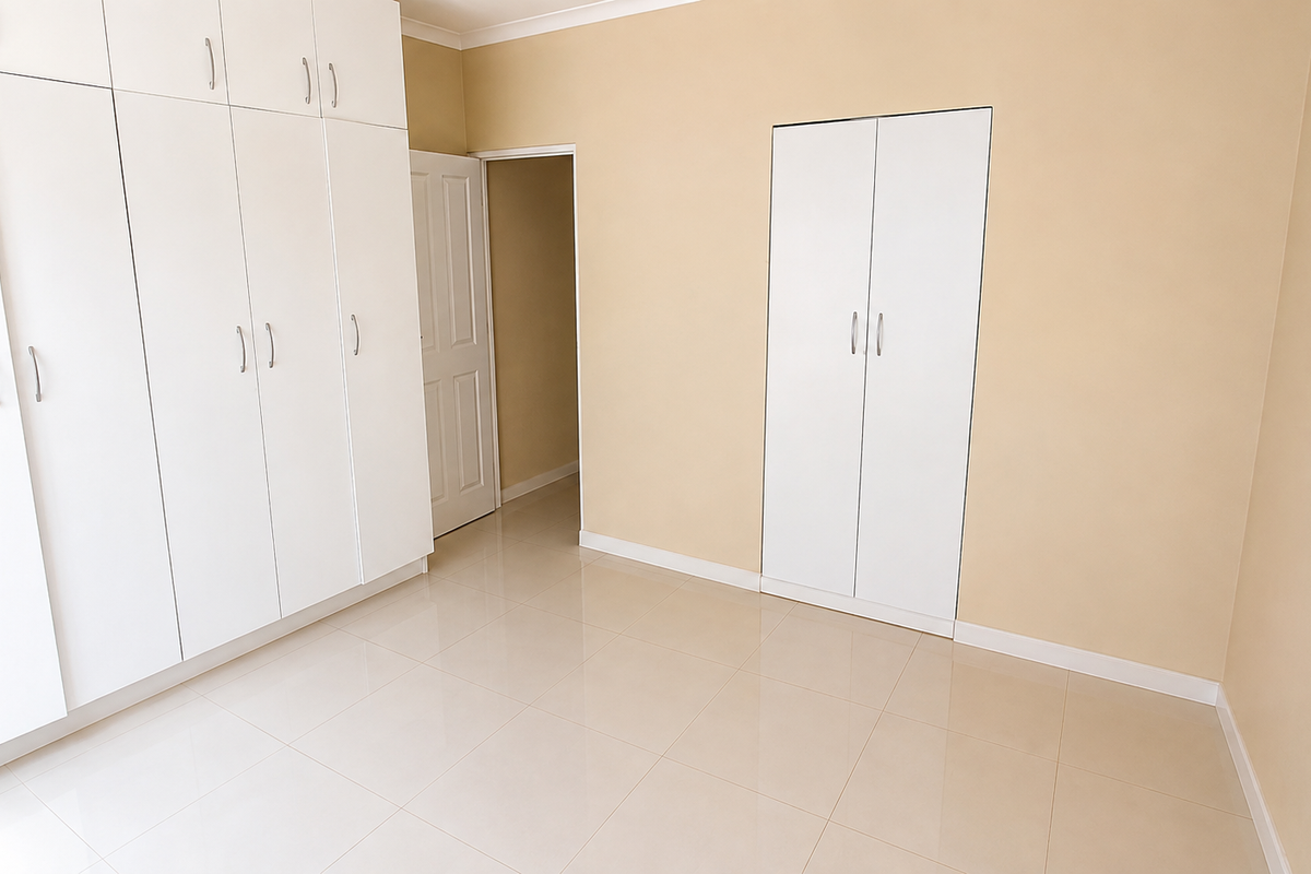 A bright, empty bedroom featuring extensive built-in white cabinetry, neutral wall tones, and clean tiled flooring throughout.
