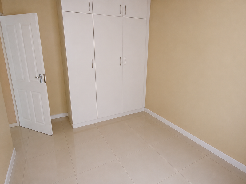 A clean, empty bedroom featuring neutral wall tones, tiled flooring, and white built-in cupboards, offering a blank canvas for personalization.