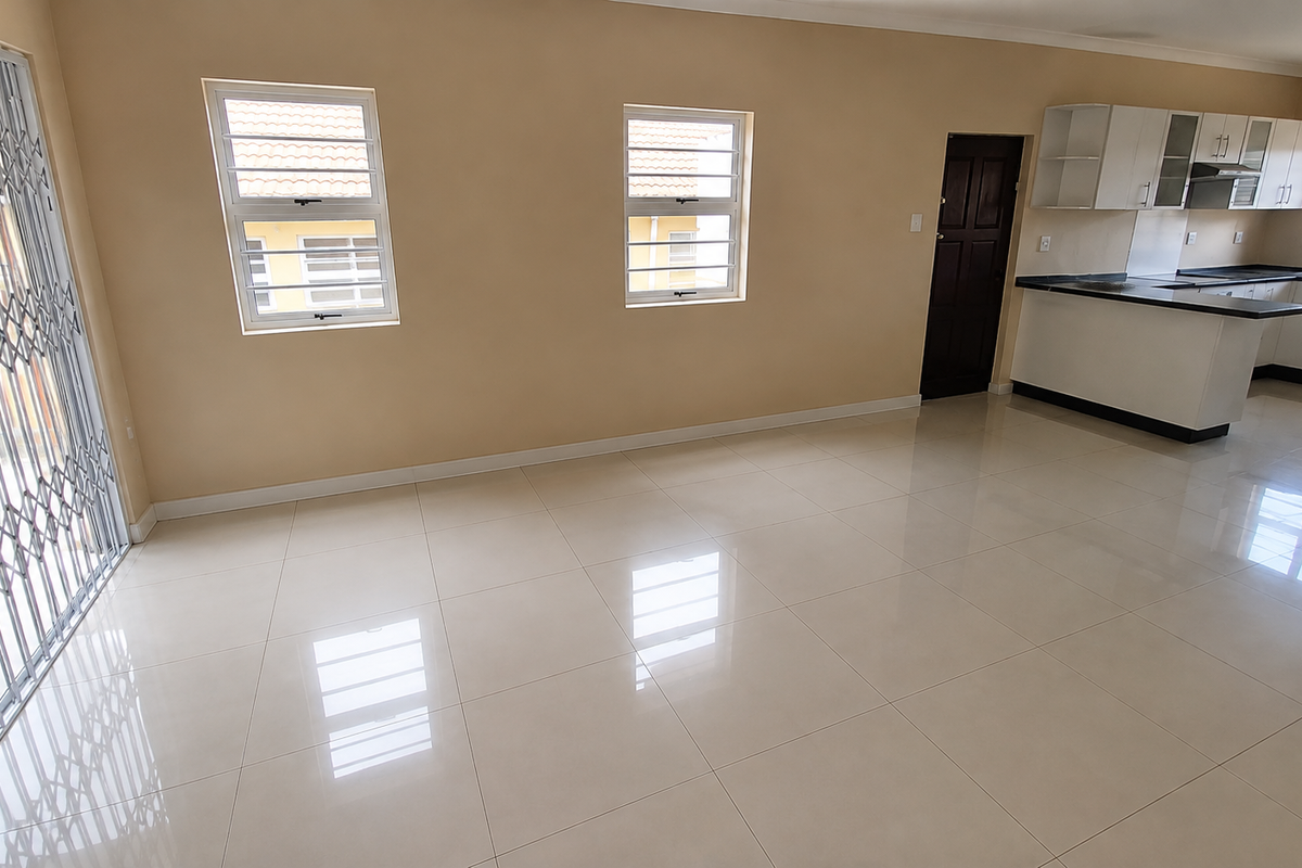 Spacious open-plan living area featuring polished tile flooring, a modern kitchen with built-in cabinetry, and a secure sliding door leading to the exterior.
