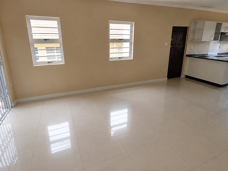 Spacious open-plan living area featuring polished tile flooring, a modern kitchen with built-in cabinetry, and a secure sliding door leading to the exterior.