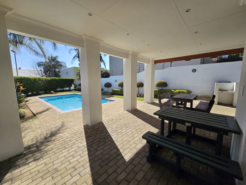 A spacious covered patio featuring paved flooring and recessed lighting, overlooking a private swimming pool and a well-maintained garden area.