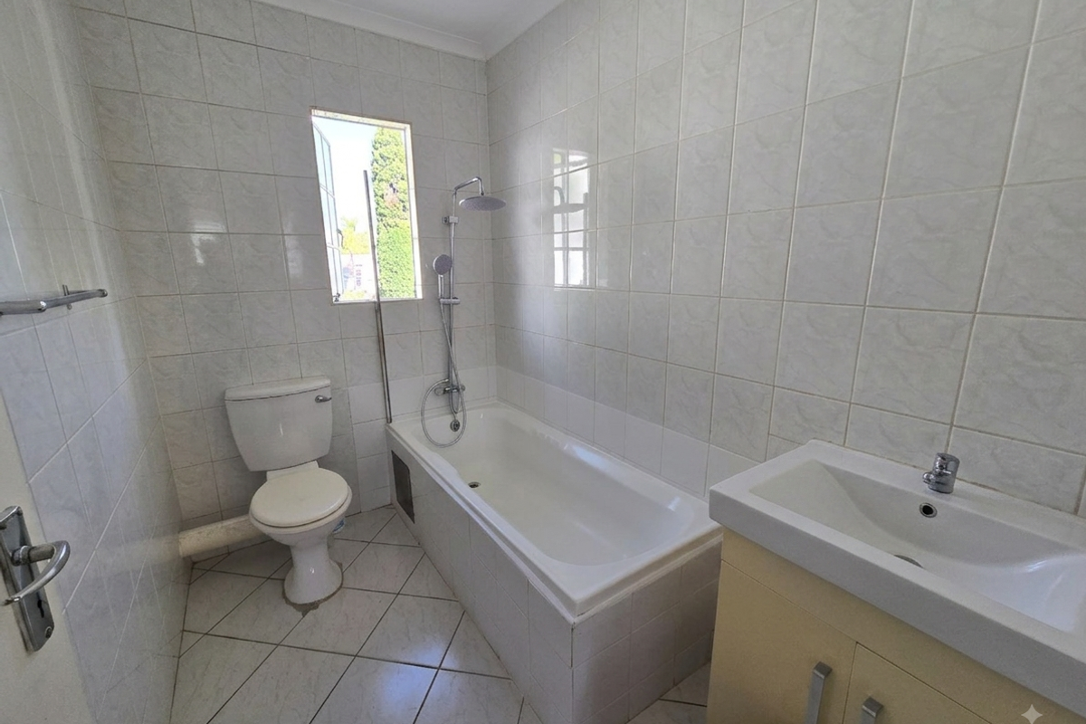 A functional bathroom featuring a bathtub with shower attachment, a vanity basin, and a toilet, finished with neutral wall and floor tiling.