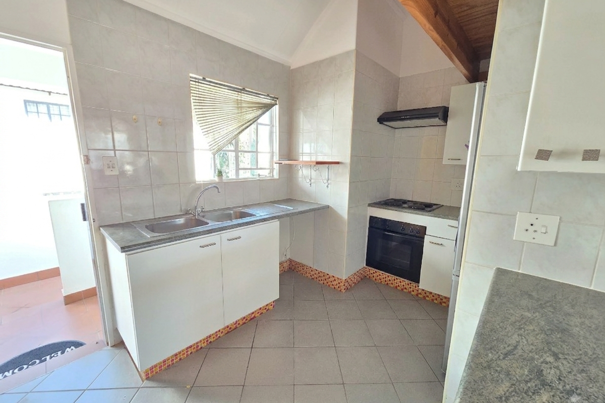 A functional kitchen featuring built-in cabinetry, a double basin sink, integrated oven and hob, and exposed timber ceiling beams with tiled flooring.