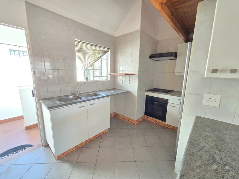 A functional kitchen featuring built-in cabinetry, a double basin sink, integrated oven and hob, and exposed timber ceiling beams with tiled flooring.