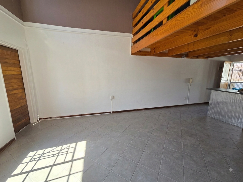 An open-plan living area featuring tiled flooring, a wooden mezzanine loft structure, and direct access to an exterior security gate.