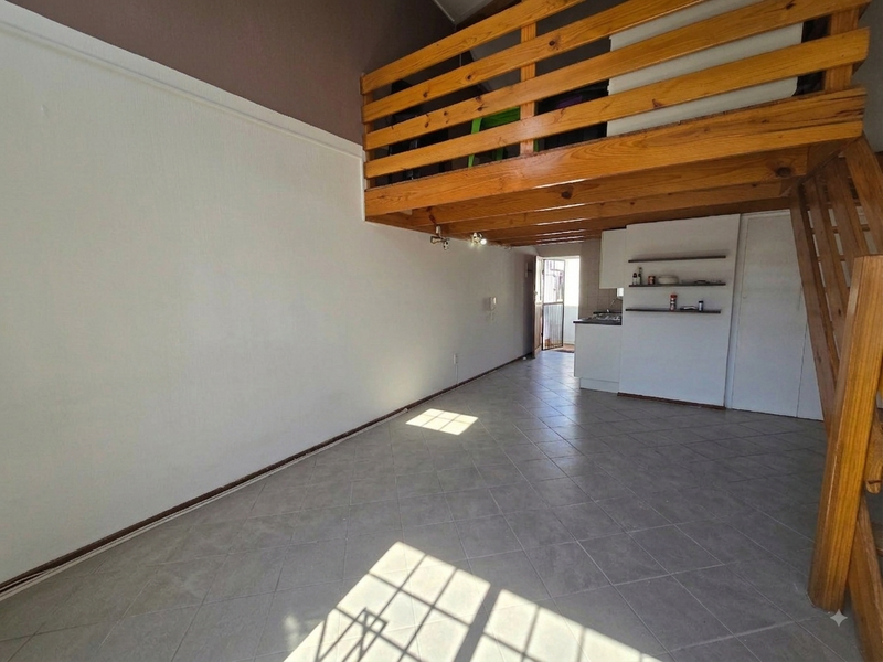 Open plan living area featuring a mezzanine level with wooden staircase and balustrade, tiled flooring, and a compact kitchenette with built-in shelving.