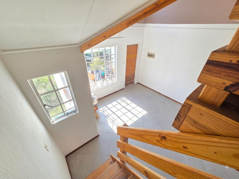 An empty hallway area featuring a wooden staircase, tiled flooring, and natural light from grid windows.