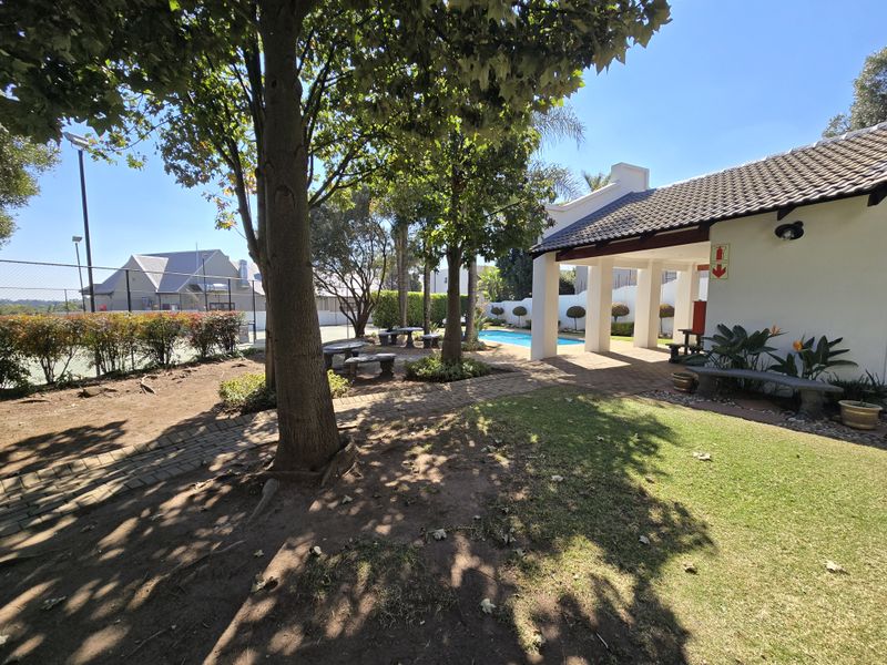 Outdoor communal area featuring a swimming pool, covered patio, and tennis court within a well-maintained residential complex setting.