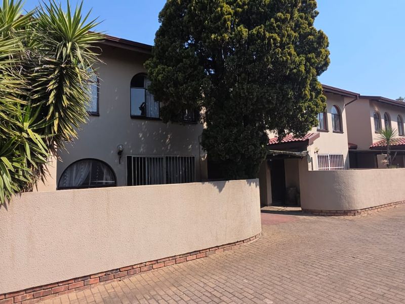 Front exterior view of a townhouse complex featuring a paved driveway, boundary walls, and arched window detailing.