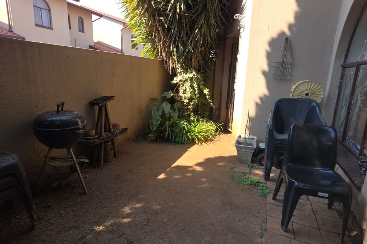 A rear courtyard area featuring a boundary wall, arched window access, and an unpaved ground surface requiring landscaping improvements.