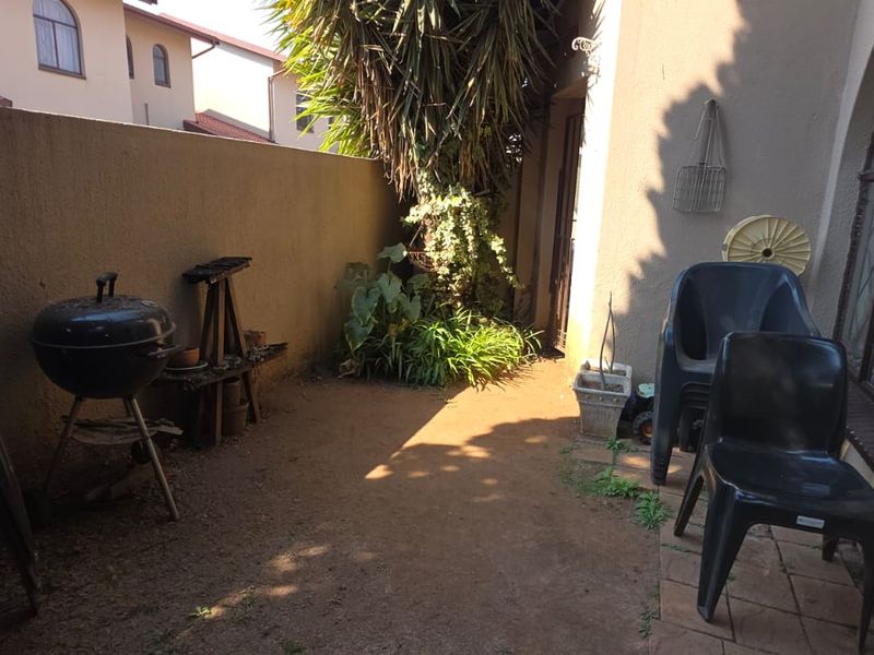 A rear courtyard area featuring a boundary wall, arched window access, and an unpaved ground surface requiring landscaping improvements.